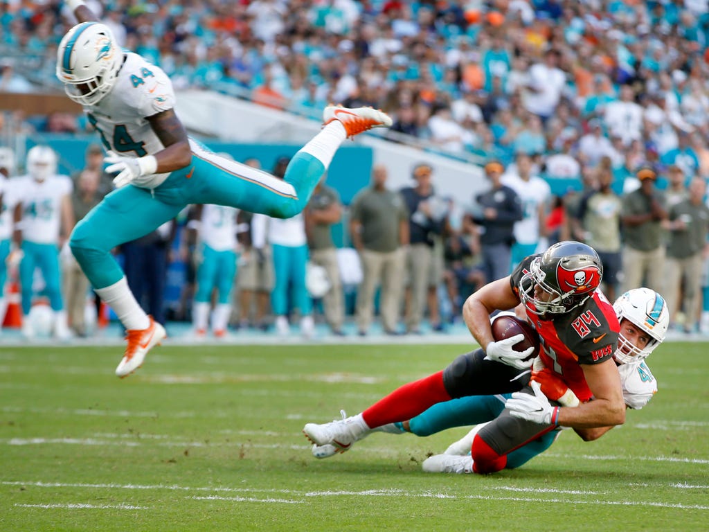 Miami Dolphins outside linebacker Stephone Anthony, left, leaps over middle linebacker Kiko Alonso, right,  who tackles Tampa Bay Buccaneers tight end Cameron Brate during the quarter  at Hard Rock Stadium.