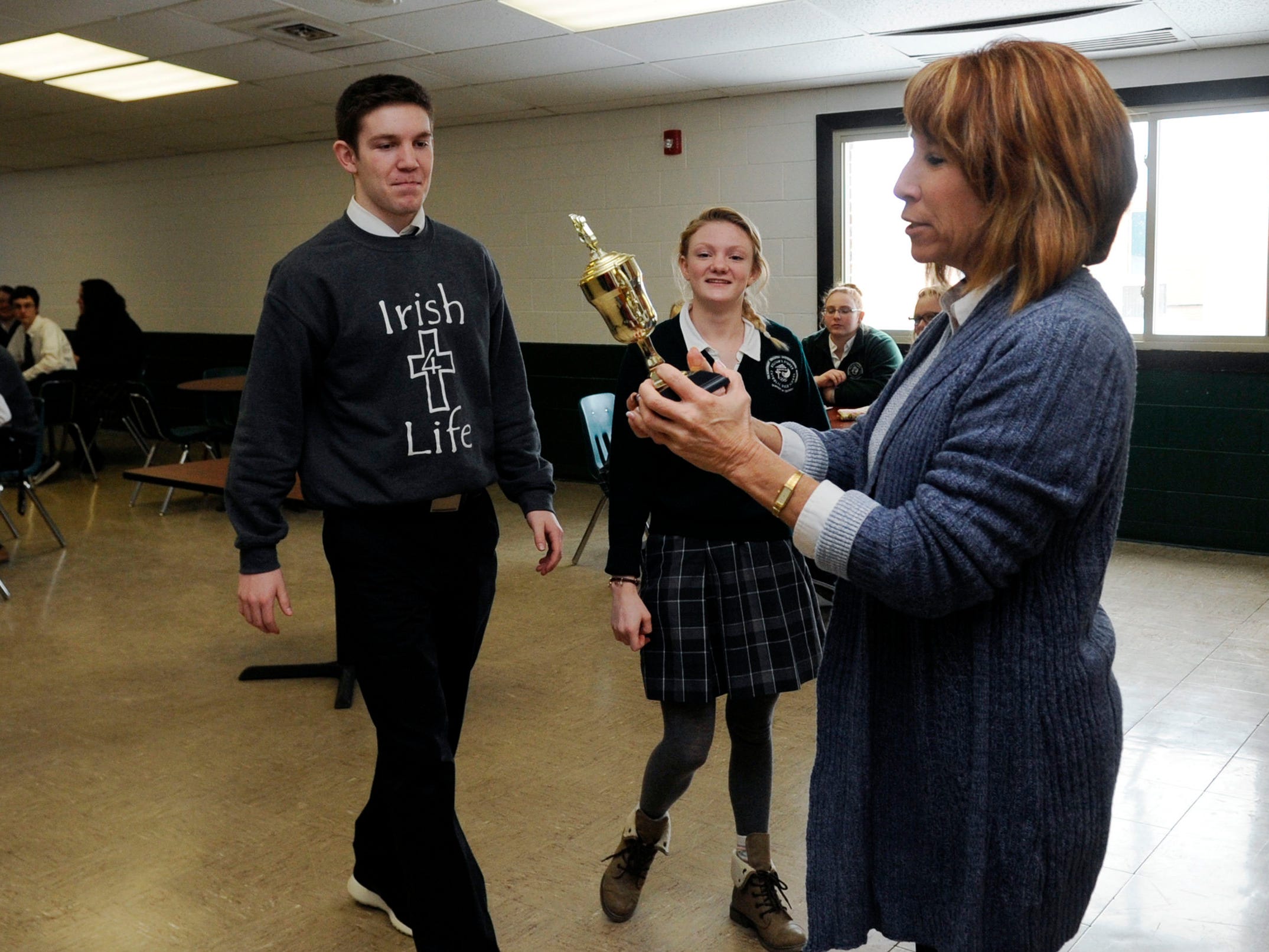 Fisher Catholic principal Maureen "Mo" Beck presents the 2015 Lancaster Eagle-Gazette Battle of the Fans Champion trophy to Eli Frazier, left, and Adriana DeGenova, center, Wednesday at Fisher Catholic High School in Lancaster.