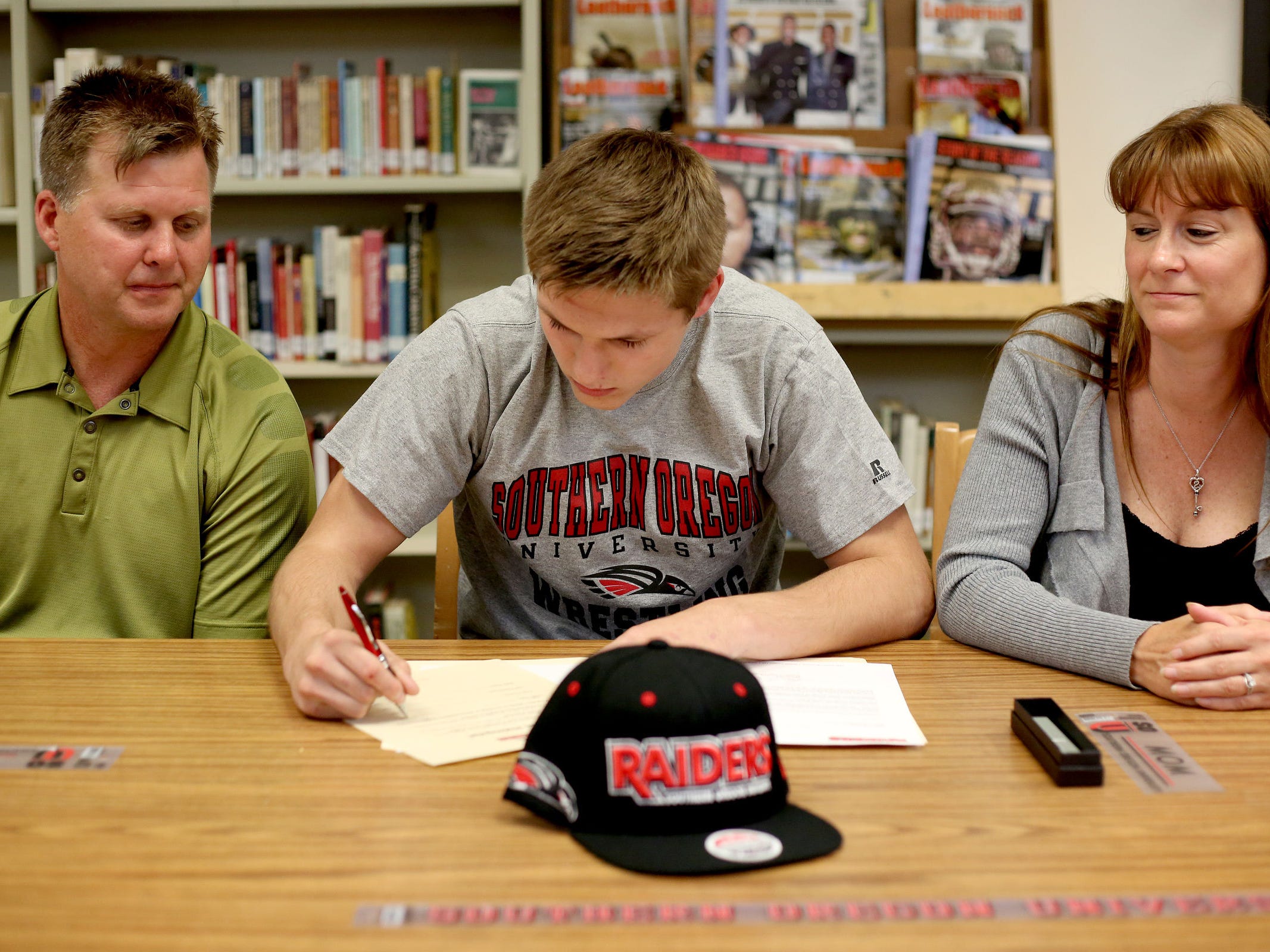 Logan Holmquist signs a letter of intent to wrestle at Southern Oregon, sitting between his parents, Dave Holmquist and Chrissy Borregard, during a signing day ceremony Monday, May 18, at Sprague High School.