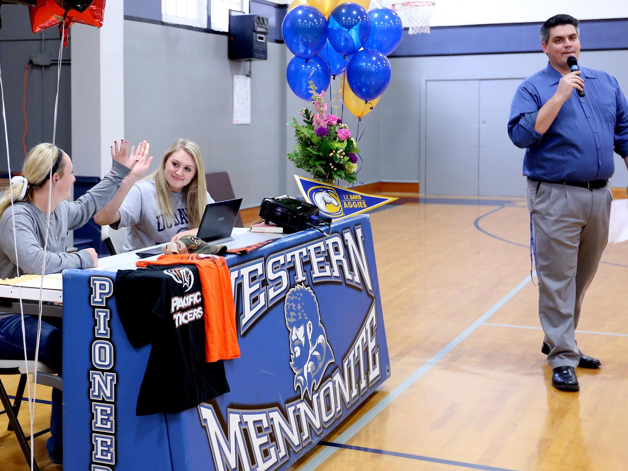 Maddie Hopper and Emma Gibb, center, high five while girl's basketball coach Robby Gilliam introduces them before they sign letters of intent to play softball with the University of the Pacific and basketball at UC Davis, respectively, at Western Mennonite High School in Salem on Wednesday, Nov. 11, 2015.