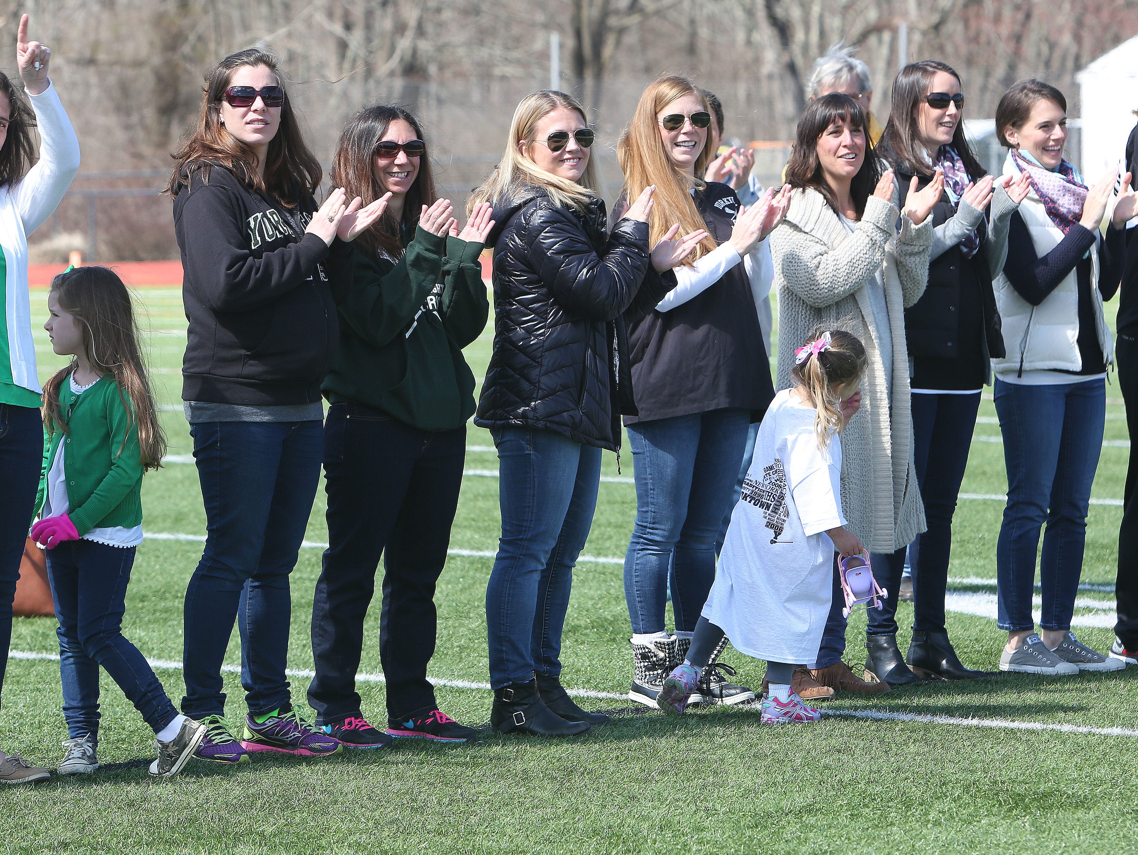 Former Yorktown girls lacrosse players wave to the crowd as they are introduced during a halftime ceremony honoring the 1996 and 2006 state championship teams at Yorktown High School during Saturday's game against Arlington.