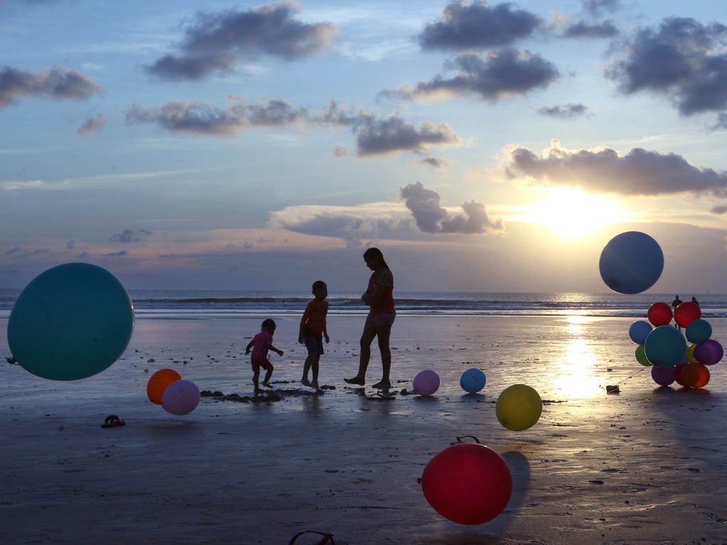 A mother plays with her children on the beach during sunset in Bali, Indonesia.