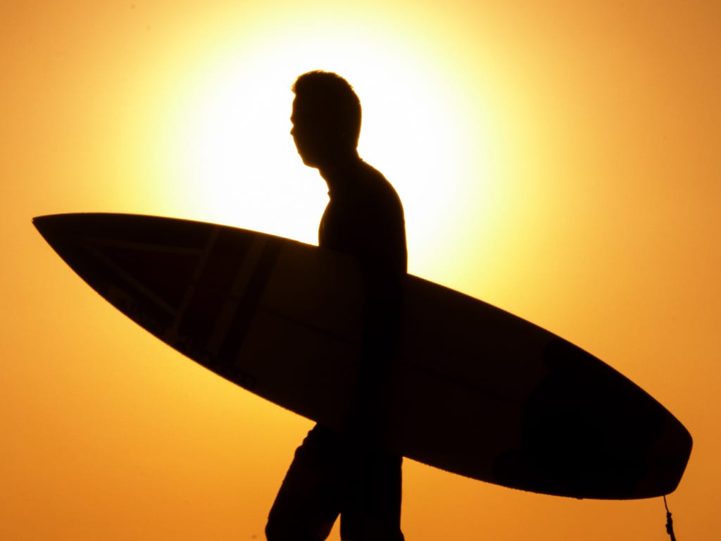 A surfer walks on the beach in the Israeli coastal city of Netanya, north of Tel Aviv, as the sun sets over the Mediterranean Sea.