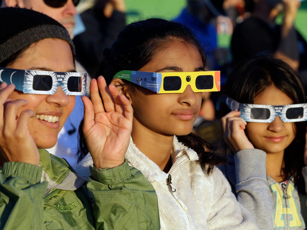 From left, Schweta Kulkarni, Rhea Kulkarni and Saanvi Kulkarni, from Seattle, try out their eclipse glasses on the sun at a gathering of eclipse viewers in Salem, Ore., early  Aug. 21, 2017.