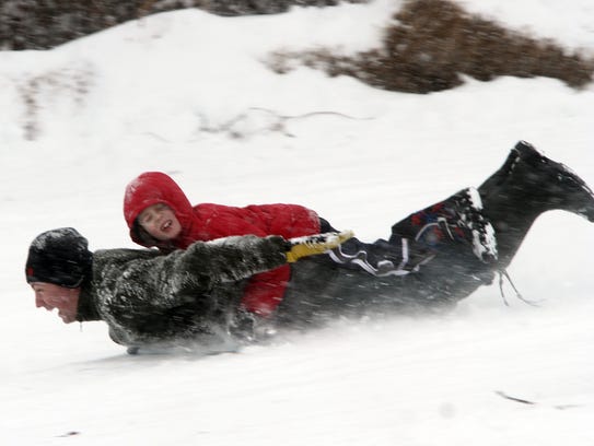 Sledders speed down a snowy hill at Donaldson Park
