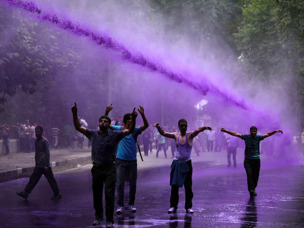 Kashmiri daily-wage and contractual government employees shout slogans as Indian police spray purple-colored water  to disperse them during a protest march in Srinagar, the summer capital of Indian Kashmir.