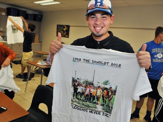 Vadiel Vazquez, catcher with the Heritage High baseball team, shows off his Sandlot t-shirt given to him by David Evans, of New Smyrna Beach, writer, director and narrator of "The Sandlot," signed autographs for the Heritage High Baseball team before their 14th game Monday afternoon. Evans paid a surprise visit to the team after hearing about their wager with their coach; if they win all 14 of their games, they could name his baby. The team came up with the name Benjamin Smalls, from a character in the movie The Sandlot."