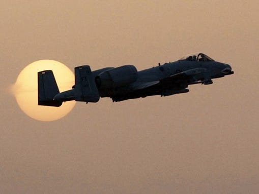 An A-10 fighter takes off past the setting sun during