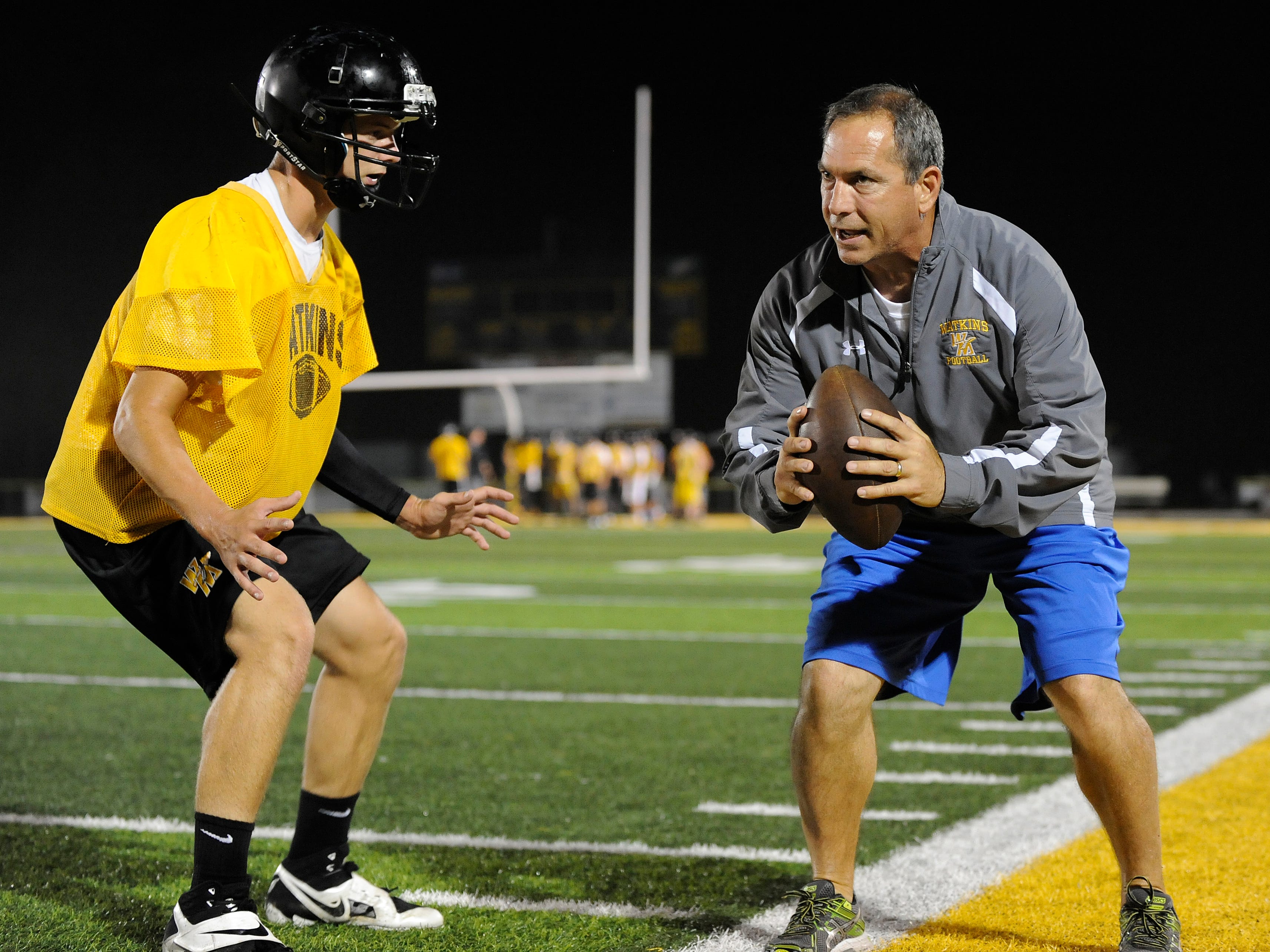 Watkins Memorial football coach Jeff Severino, right, runs Cole Nixon through a secondary drill during the Warriors’ midnight practice this past August. Severino said the Warriors are operating as usual in advance of the upcoming vote on the critical renewal levy.