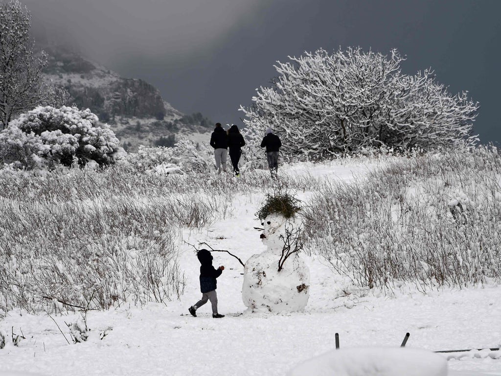 A child plays in the snow next to a snow man, by the road called route de la Gineste, connecting Marseille and Cassis, on Dec. 2, 2017, outside Marseille, southern France.