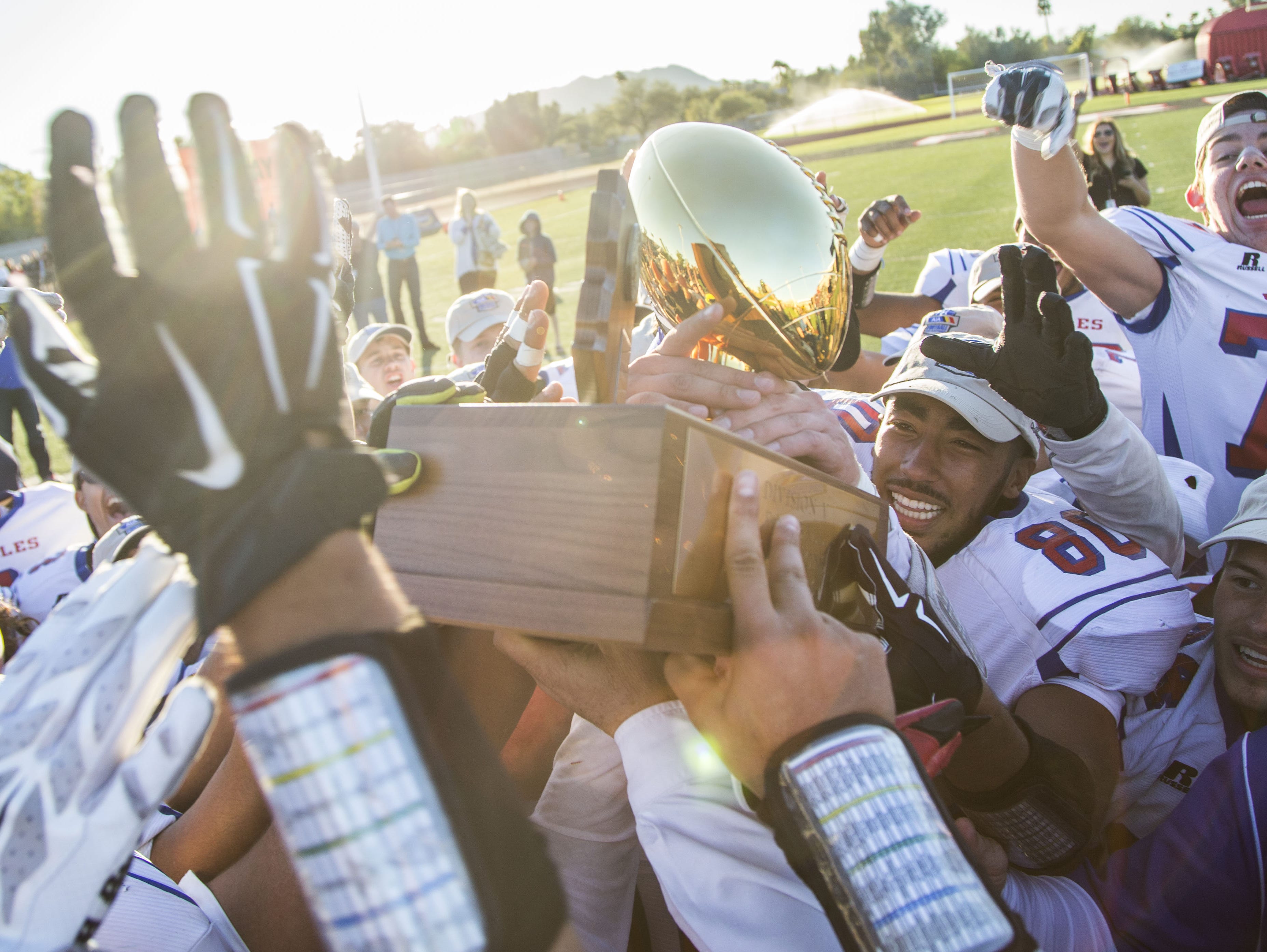 Joy Christian's Isaiah Goodspeed (80) lifts the trophy with his teammates after winning the Division V State Championship against Benson at Chaparral High School on Nov. 28, 2015 in Scottsdale Ariz.