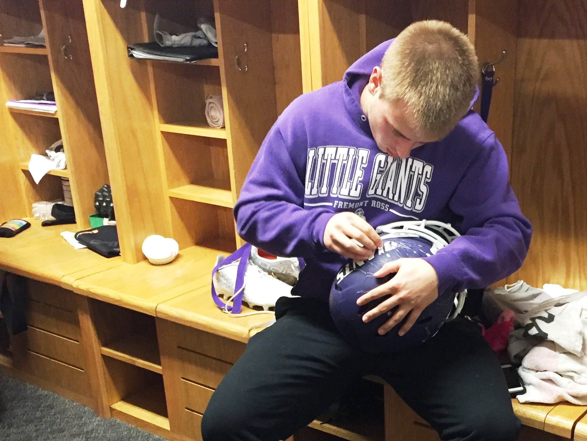 Fremont Ross senior Sam Detwiler sits at his locker stall and peels the stickers from his helmet Monday afternoon.