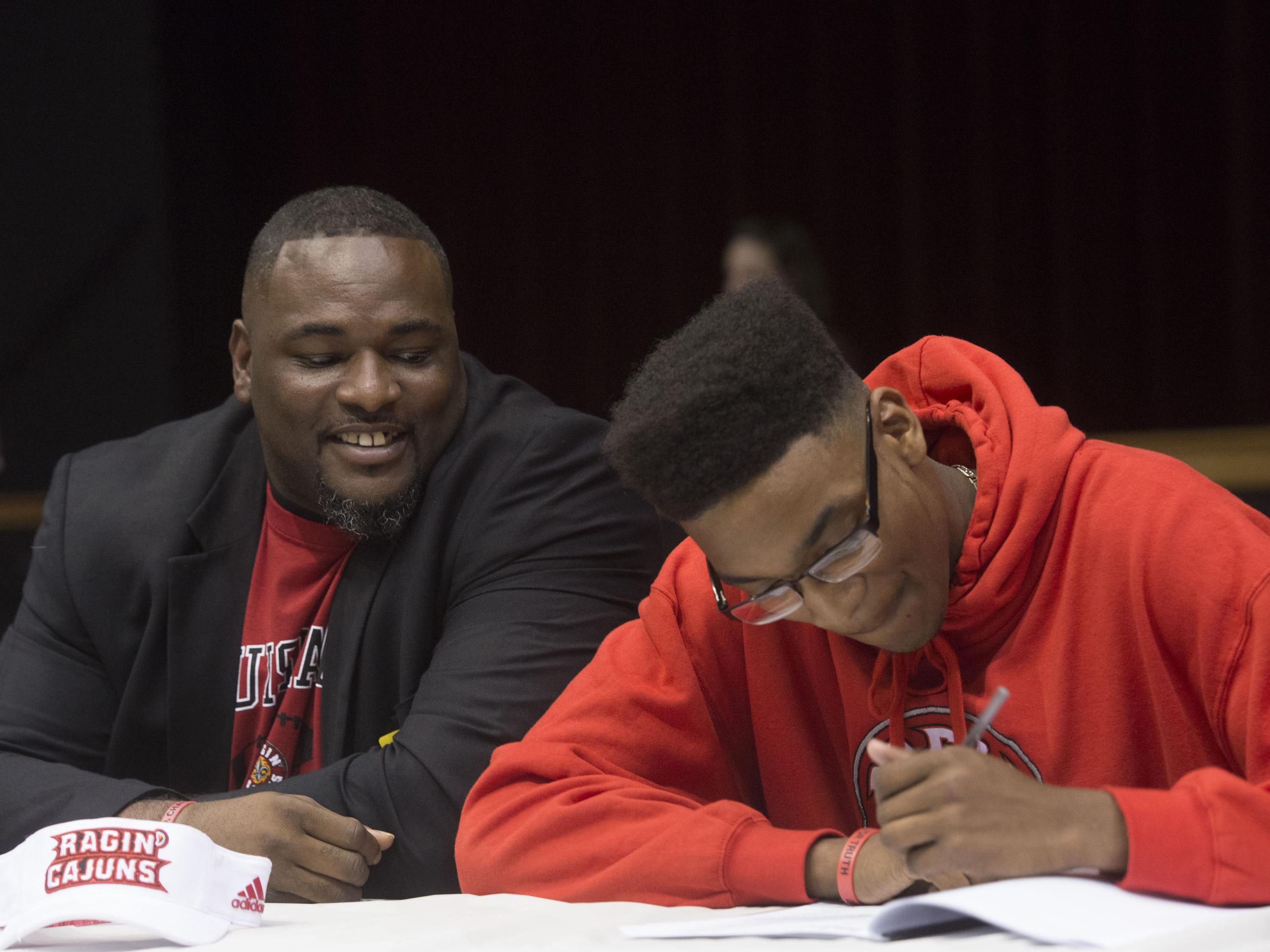 Pensacola High School's Calif Gossett, right, signs a commitment letter to University of Louisiana at Lafayette during national signing day while his stepfather Anthony Crenshaw, left, looks on