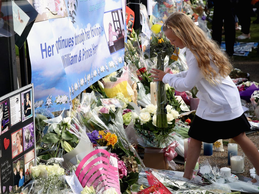 A young girl lays flowers at the Gates of Kensington Palace on the 20th anniversary of the death of Princess Diana at Kensington Palace in London.