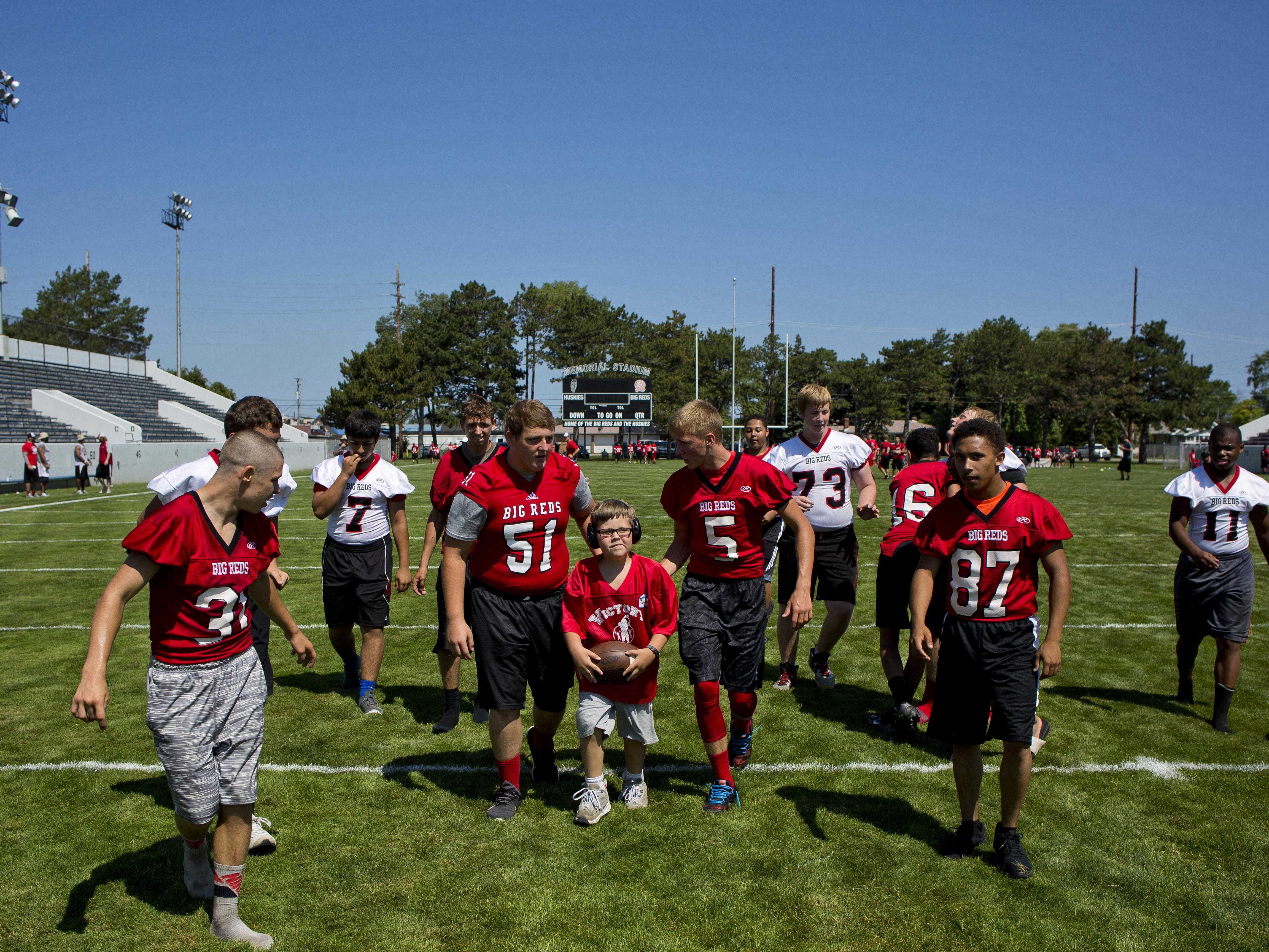 Johnathan Larson, center, is cheered on as he runs the ball down field during Victory Day Saturday, August 15, 2015 in Memorial Stadium at Port Huron High School. The event paired special needs students with mentors from the football and cheerleading teams.