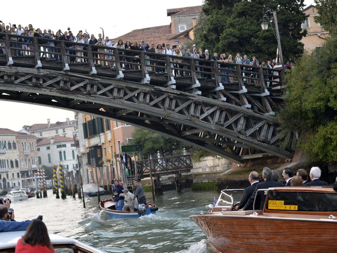 People watch from a bridge as George Clooney passes  on a taxi boat.