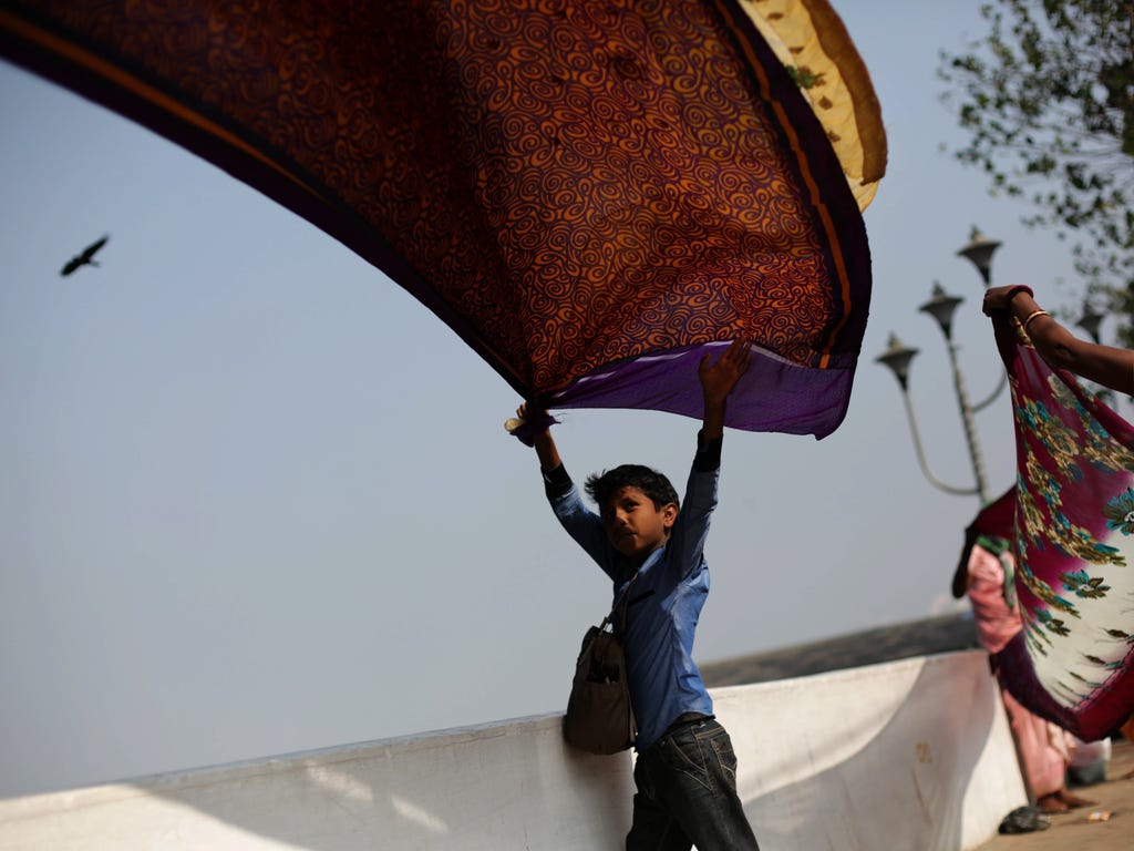 A boy holds a saree to dry under sunlight  on the bank of river Ganga near Babughat transit camp as the religious gathering ahead of Ganga Sagar annual fair in Kolkata, India. The Fair is an annual gathering to take a dip in sacred waters of Ganga Ri