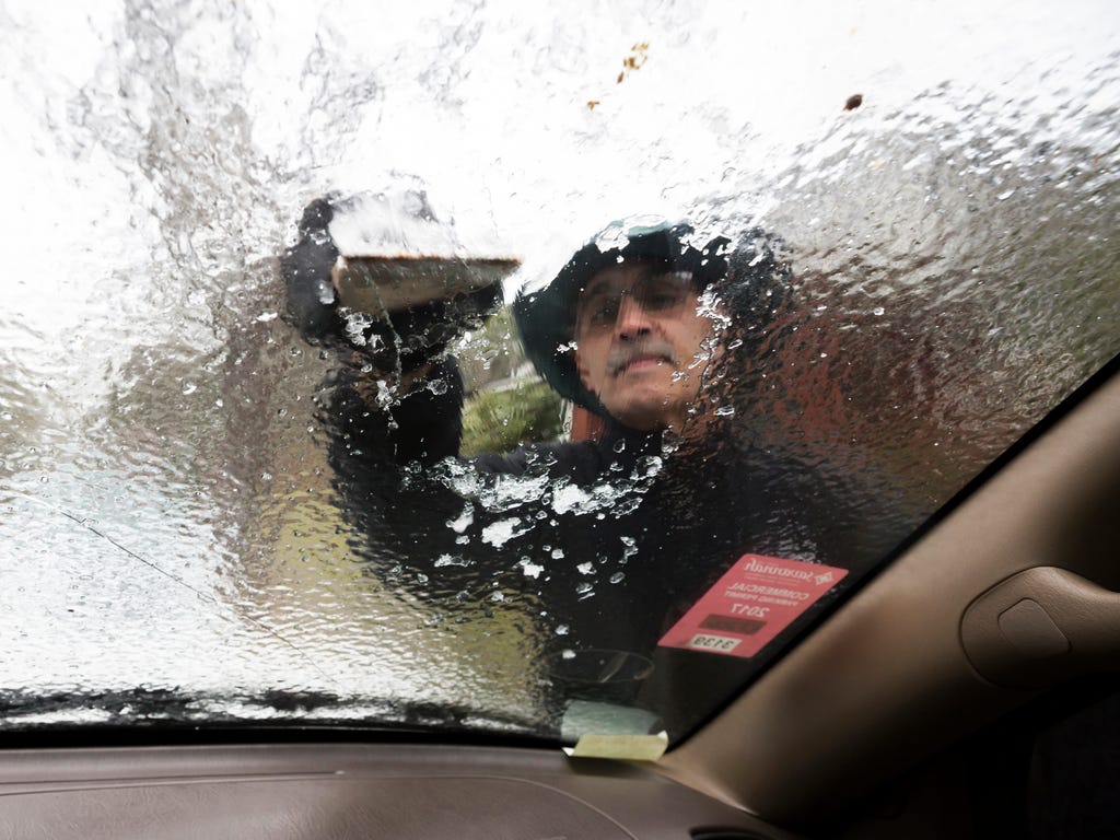 Omar Elkhalidi uses a wood shim to scrape ice off his windshield that accumulated overnight from freezing temperatures, Jan. 3, 2018, in Savannah, Ga.