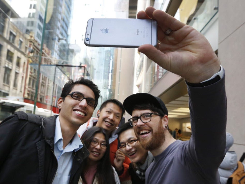 A file photo dated 25 September 2015 showing an Apple employee taking a 'selfie' photograph of some people with the new iPhone 6s phone, as they stand in a queue inside the Apple store in Sydney, Australia,