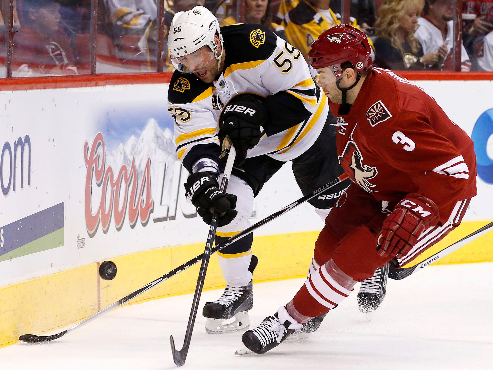 Boston Bruins' Johnny Boychuk (55) and Phoenix Coyotes' Keith Yandle (3) battle for the puck during the first period of an NHL hockey game on Saturday, March 22, 2014, in Glendale.