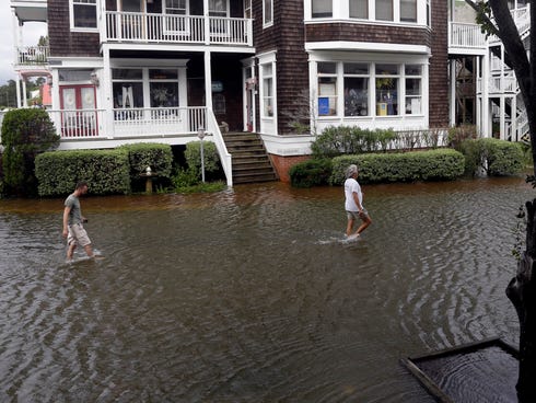 People walk along a flooded street near the waterfront in Manteo, N.C., Friday, July 4, 2014, after Hurricane Arthur passed through the area leaving some roads underwater.