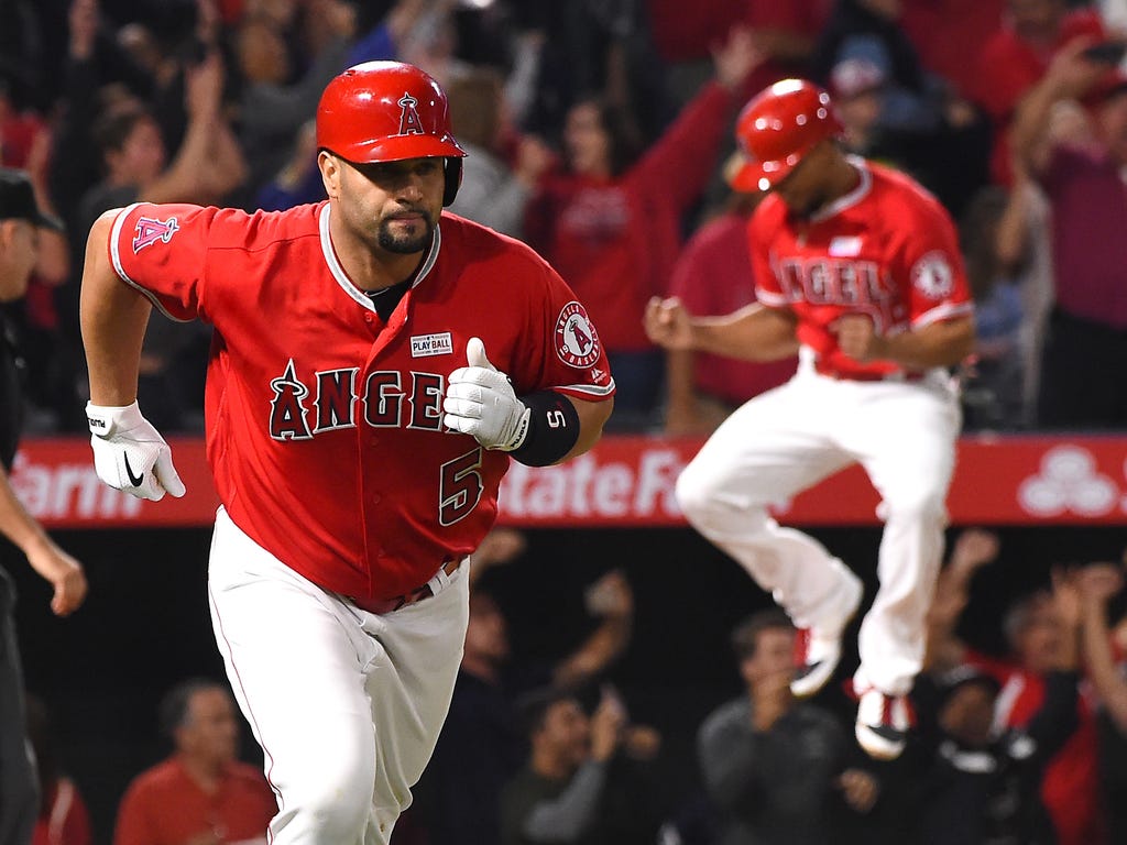 The Los Angeles Angels' Ben Revere leaps in the air as Albert Pujols rounds the bases after hitting a grand slam for his 600th career home run.