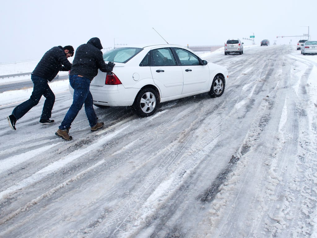 Curtis Hansen, left, and Jeff Malley push a motorist up the icy northbound off-ramp from I-25 to Baptist Road north of Colorado Springs. The storm system that dropped a foot of snow in the Rockies was making travel hazardous as it headed east, menaci
