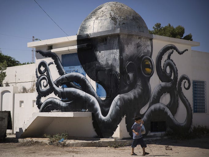 A child walks past a mural by Belgian artist ROA which decorates a wall in the village of Erriadh, on the Tunisian island of Djerba, on August 7, 2014, as part of the artistic project "Djerbahood". Artists from 34 diffrents nationalities were invited by France-based Tunisian artist Mehdi Ben Cheikh to take part in an initiative to turn Djerba's Erriadh district into an "open sky museum". AFP PHOTO / JOEL SAGET= RESTRICTED TO EDITORIAL USE, MANDATORY MENTION OF THE ARTIST UPON PUBLICATION, TO ILLUSTRATE THE EVENT AS SPECIFIED IN THE CAPTION =        (Photo credit should read JOEL SAGET/AFP/Getty Images)