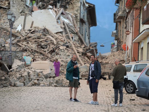 Residents stand next to damaged buildings.