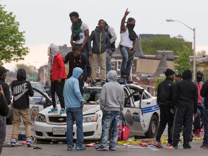 Protesters stand on a demolished police car in Baltimore.