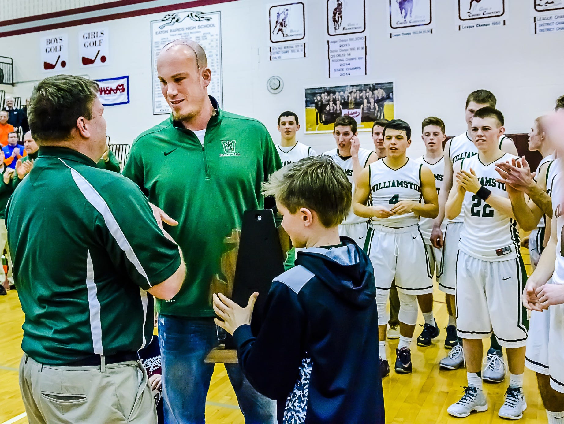 Williamston boys basketball coach Jason Bauer, second from left, accepts the Class B regional trophy after the Hornets win over Stockbridge in March at Eaton Rapids High School. Bauer has been sidelined because of brain tumors that were removed last spring.