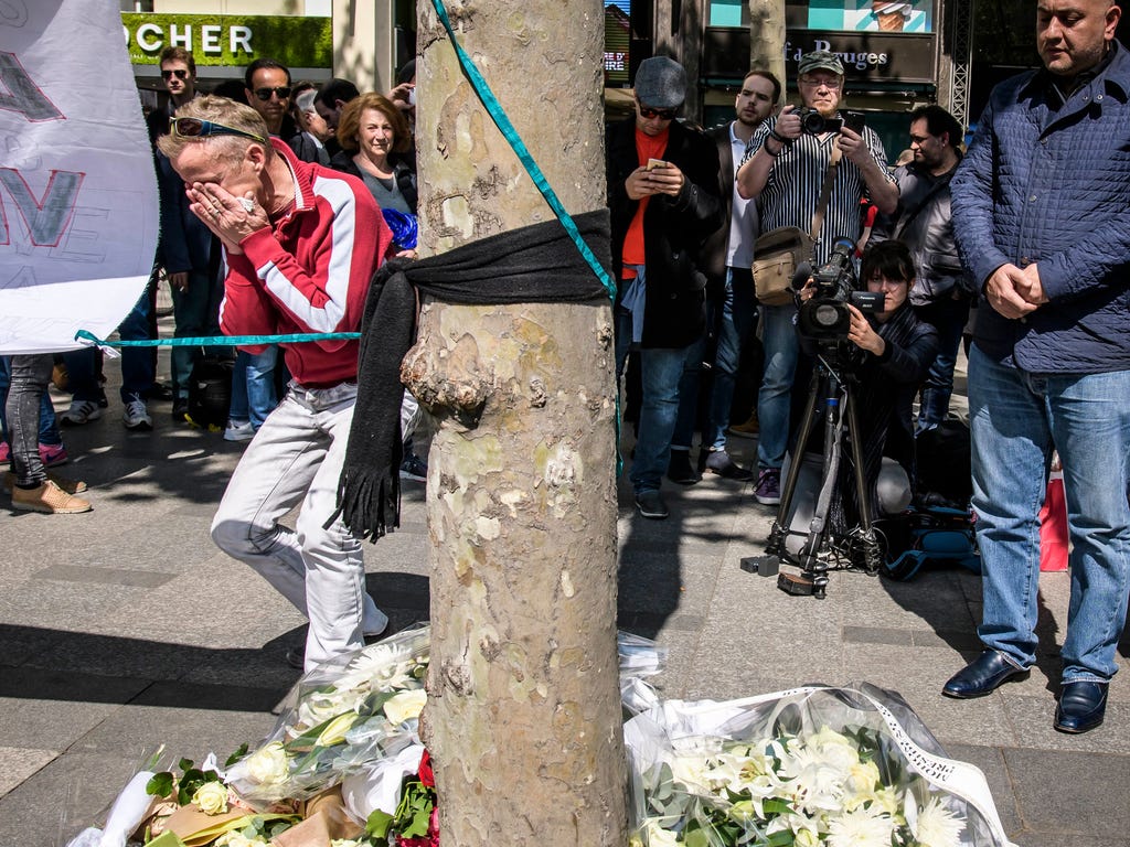 People react as they lay flowers to pay tribute to a dead French policeman at the Champs Elysee avenue in Paris,  near where he was killed in a terror attack late April 20.