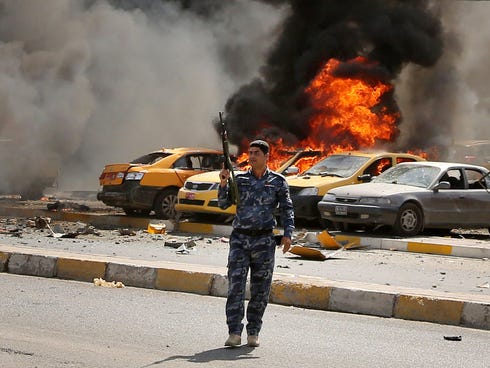 Iraqi policemen stand near burning vehicles moments after one in a series of bombs hit the Shiite stronghold of Sadr City, in Baghdad, May 13, 2014.