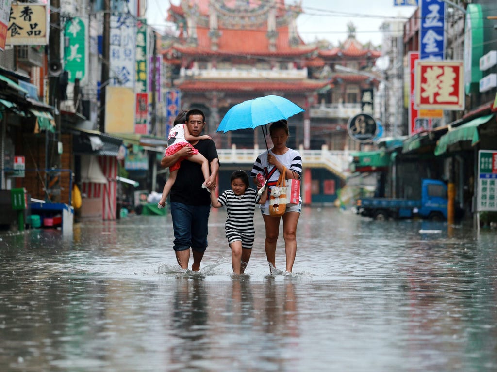 A family walks in floodwaters as Typhoon Nesat hits Pingtung county in southern Taiwan on July 29, 2017.  Taiwan came to a standstill on July 29 with power knocked out for part of the island as it braced for its first typhoon of the year.