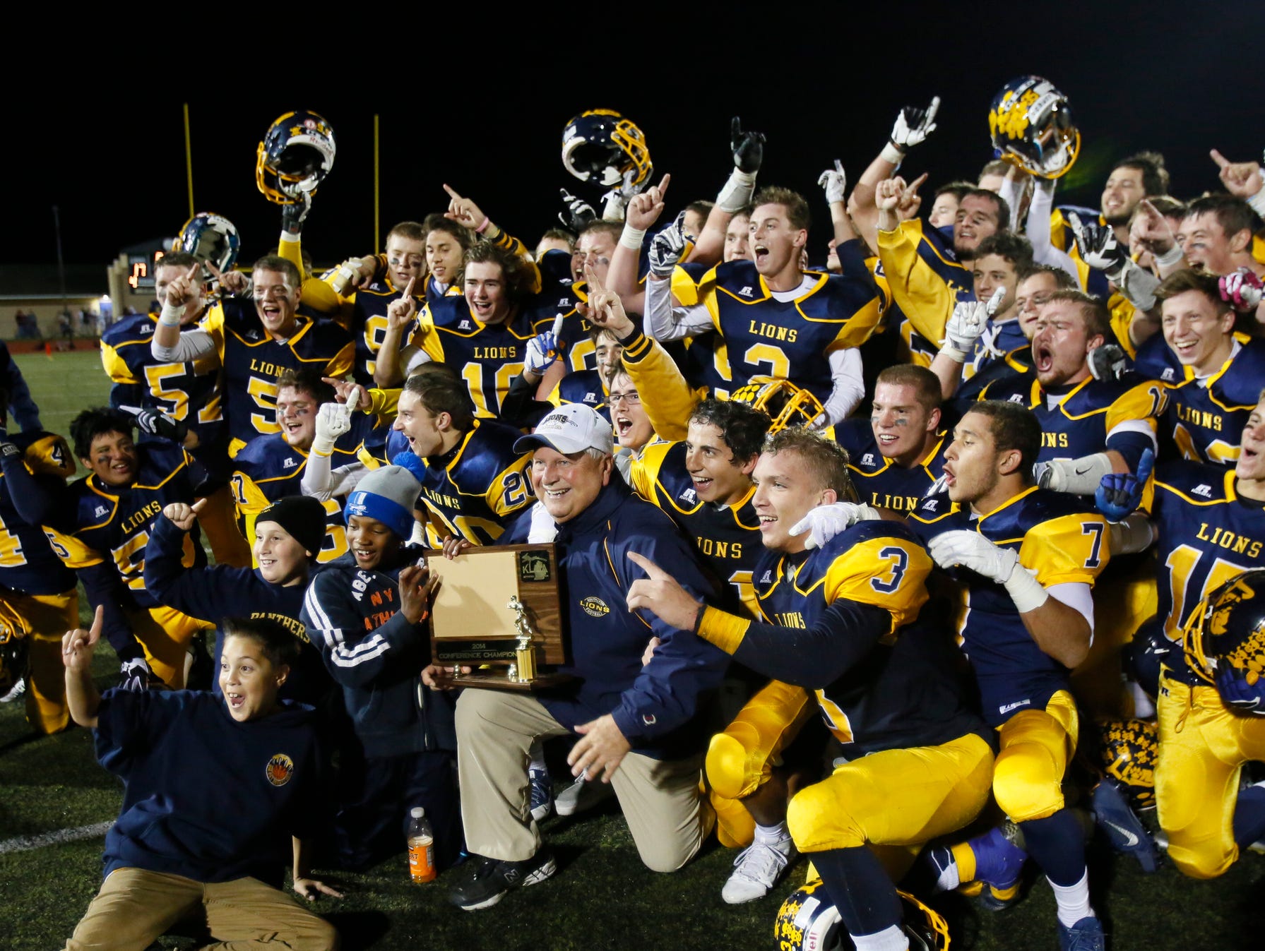 South Lyon coach Mark Thomas holds the district championship trophy as he and his players pose for photos to celebrate their 17-7 win over Canton on Oct. 17, 2014.