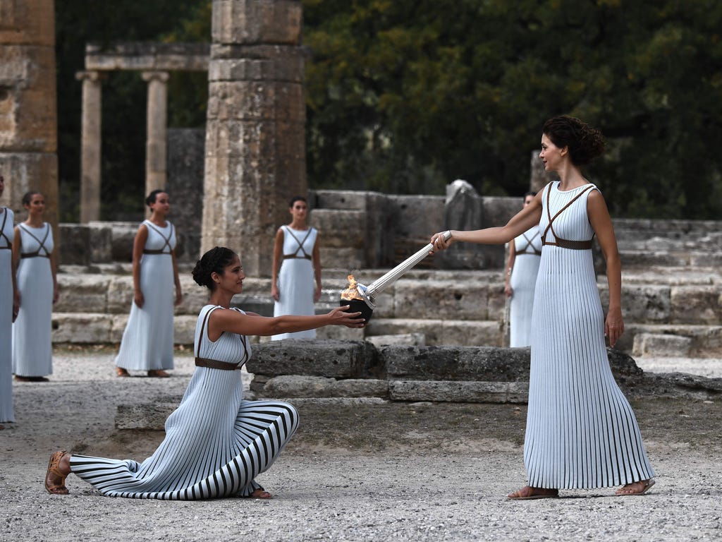 Actress Katerina Lechou, right, acting the high priestess, passes the Olympic flame at the Temple of Hera on Oct. 23, 2017, during a dressed rehearsal of the lighting ceremony of the Olympic flame in ancient Olympia, the sanctuary where the Olympic G