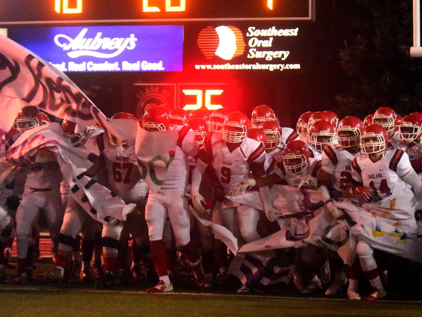 The Oakland football team breaks through a banner to run onto the field Friday.