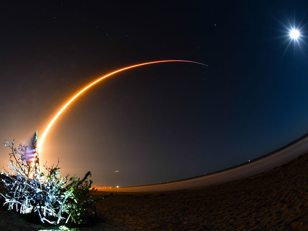 The SpaceX Falcon 9 rocket streaks across the sky with the shell tree on the beach in Cape Canaveral in the foreground and the waning gibbous moon lighting the sky. SpaceX launched a Falcon 9 rocket from Complex 40 at Cape Canaveral Air Force Station