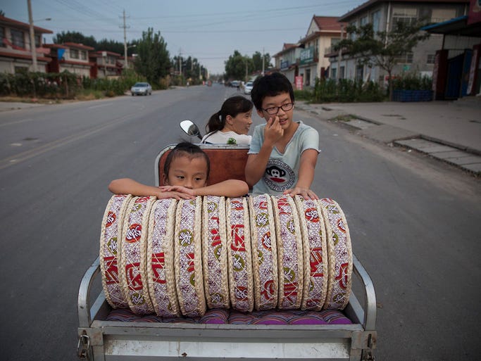 A mother transports her two daughters and straw mats to the train station in Wantou Village on Aug. 25. There are 1,000 online Taobao shops in the village and most are run by women.