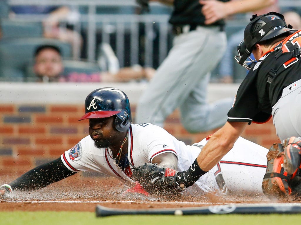 Braves runner Brandon Phillips (4) slides safely past Marlins catcher J.T. Realmuto (11) to score during the first inning in Atlanta. Phillips' run helped the Braves win 5-3.