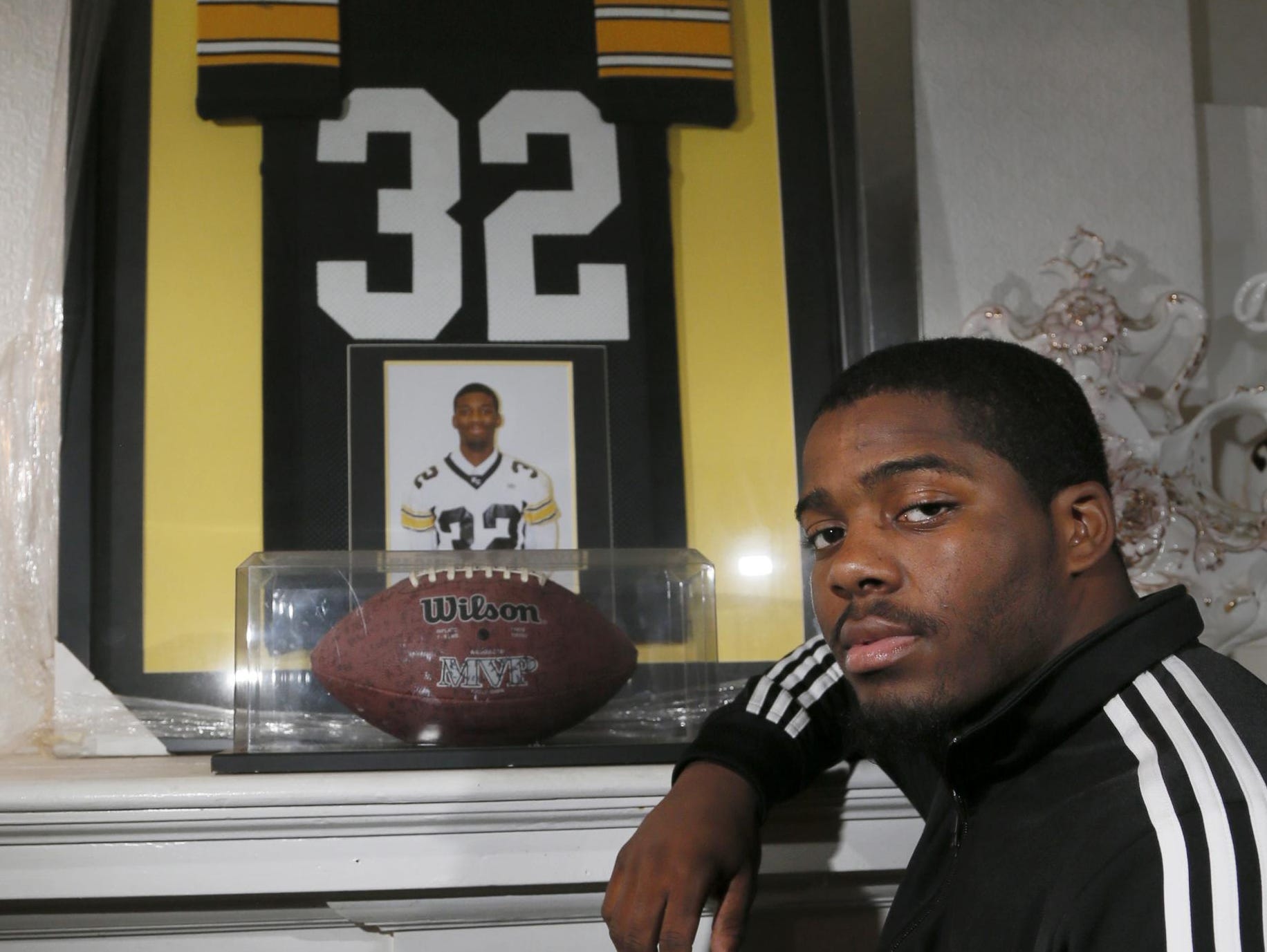 Detroit King senior running back Martell Pettaway poses with the framed jersey, photo and football from older brother, Devinne, who played for King and passed away in 2008. Pettaway wears the same No. 32.