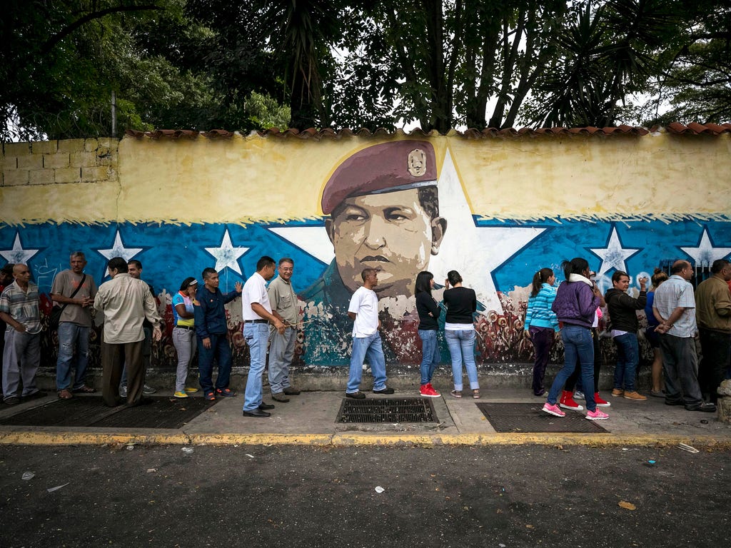 Several voters stand in a queue next to a wall with late Venezuelan president Hugo Chavez, outside a polling station in Caracas, Venezuela, on Oct. 15, 2017. Venezuelan voters are called to elect 23 new Venezuelan governors in regional elections.