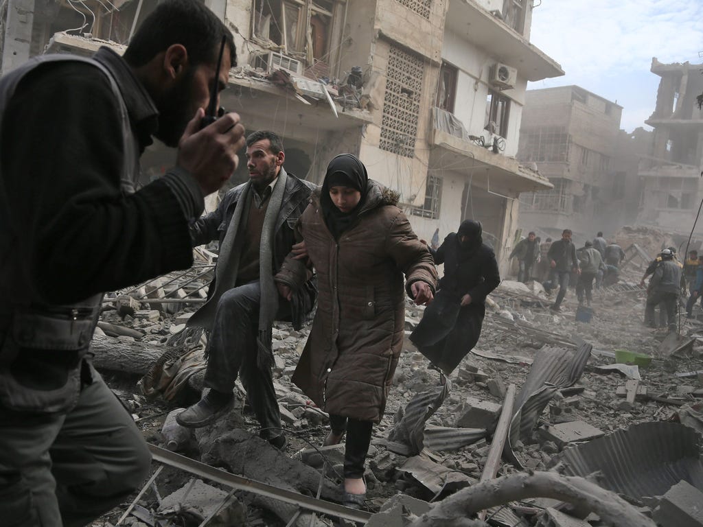 A member of the Syrian civil defense speaks on a wireless transmitter as other civilians flee from an area hit by a reported regime air strike in the rebel-held town of Saqba, in the besieged Eastern Ghouta region on the outskirts of the capital Dama