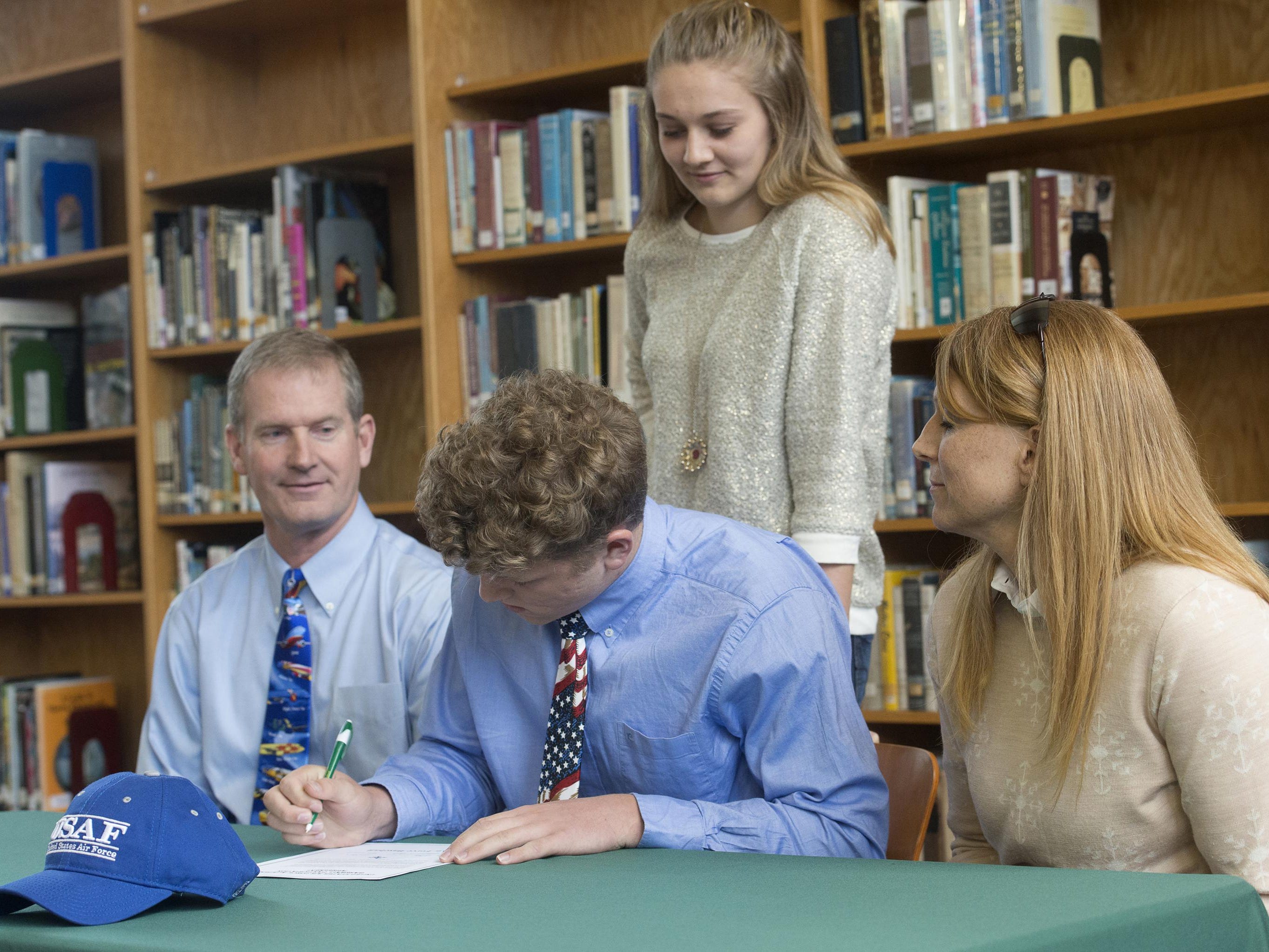 Catholic High School student, Evan Floyd, center, signs with United States Air Force Academy during a ceremony at the school Monday morning, while his family looks on.