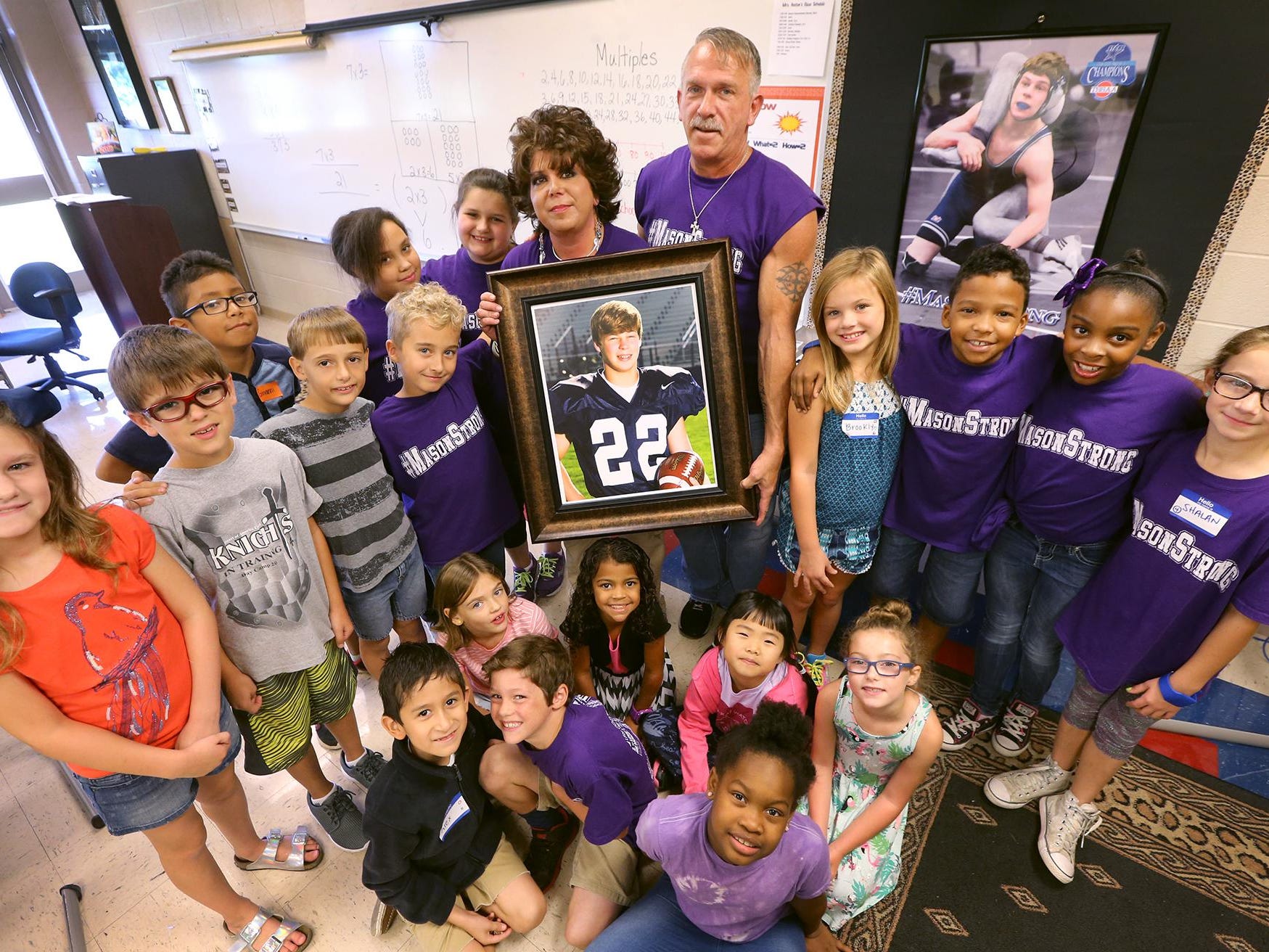 Melanie Heston and her husband, John Heston, hold a photograph of her son, Mason, who died last year. They are surrounded by her third-grade class at Scales Elementary.
