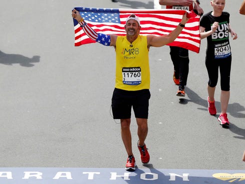 Frank Fumich of Arlington, VA holds an American flag as he crosses the finish line during the 2014 Boston Marathon.