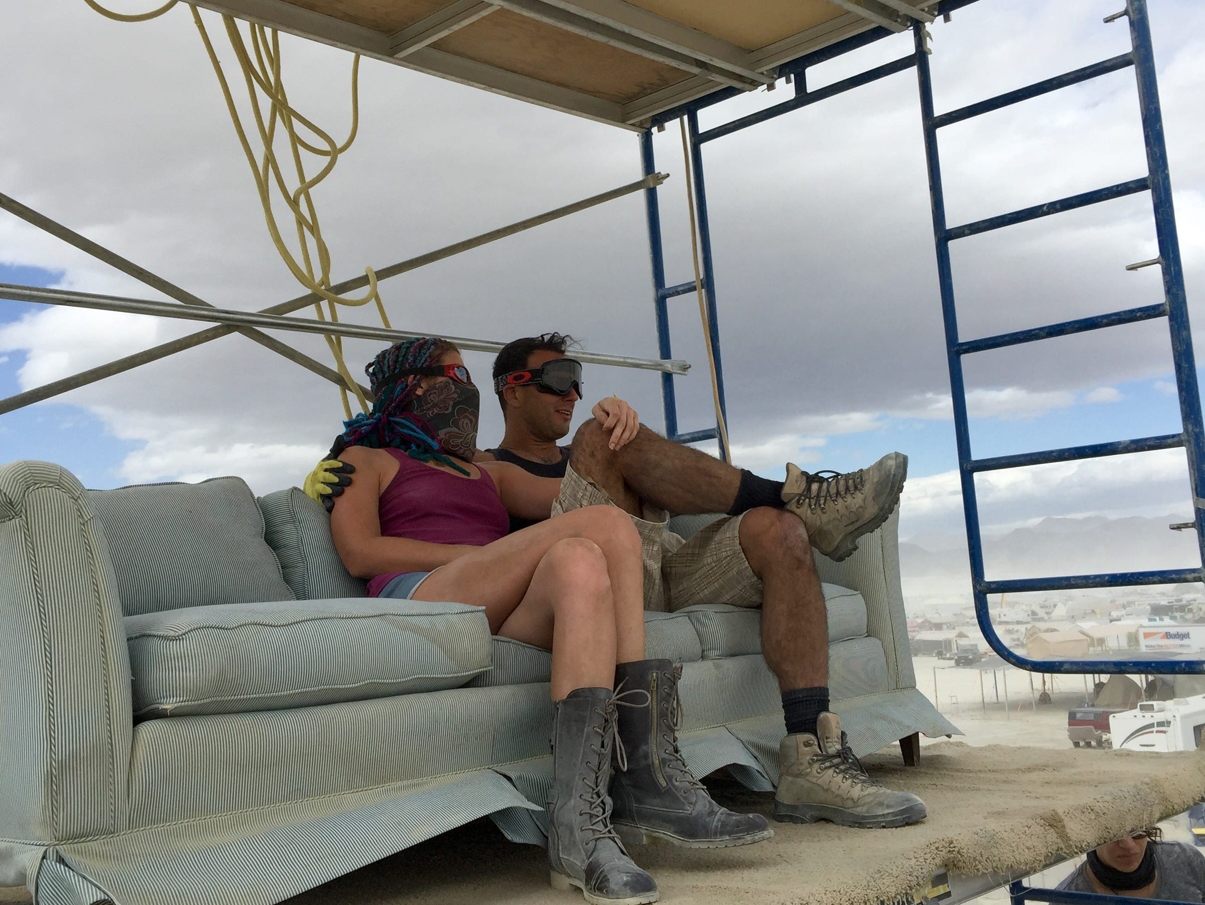 A couple relaxes during a break from work preparing for the start of Burning Man. They're sitting on a couch about 40 feet above the ground at Altitude Lounge.