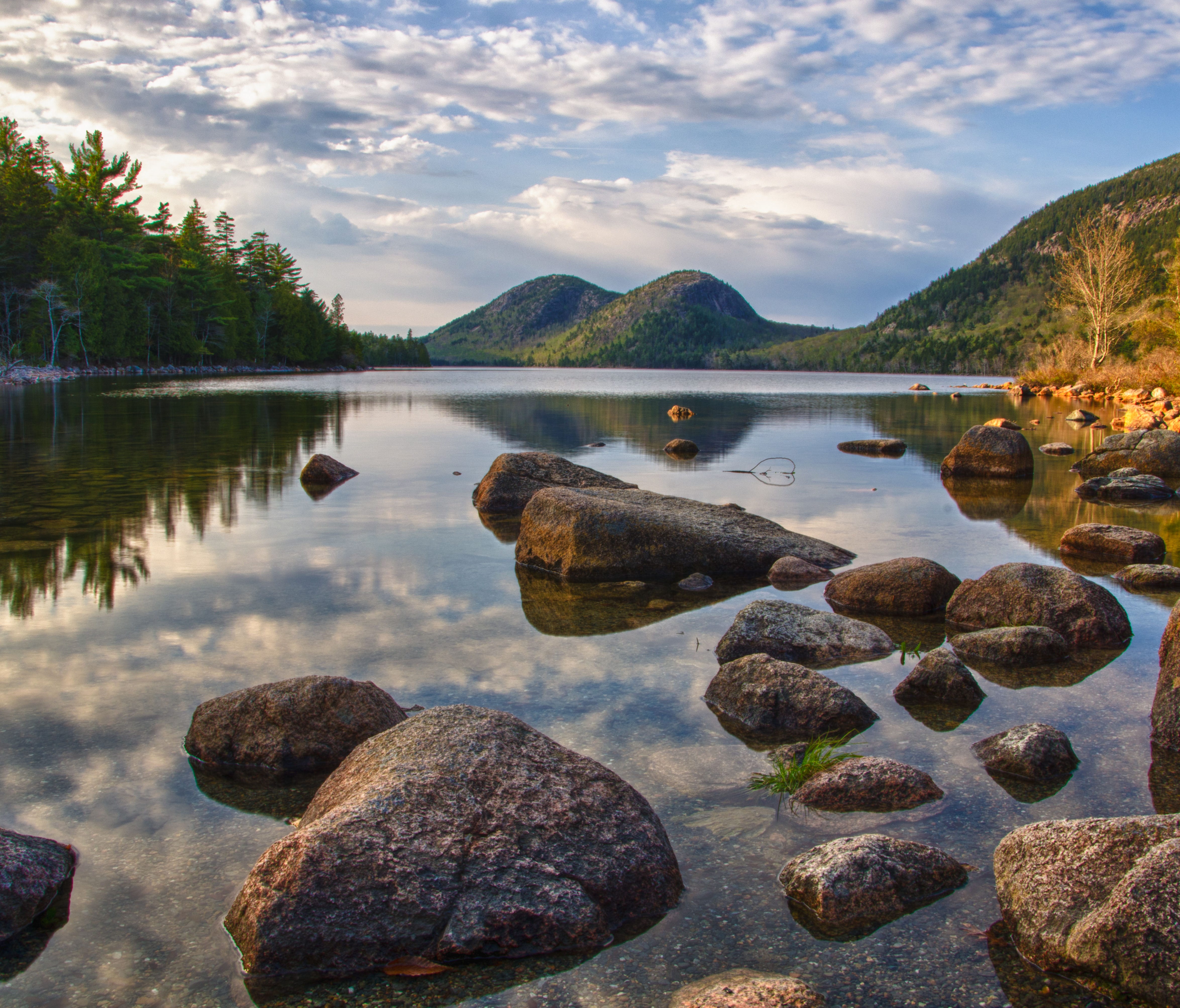 Tall trees and rolling mountains reflect in the still waters of Jordan Pond in Acadia National Park in Maine. Lakes and ponds add shimmering contrast to Acadia's forested and rocky landscape. Within or adjacent to the park, you can explore 14 great p