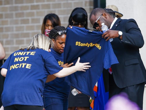 People look at a shirt with words '#SandySpeaks' printed