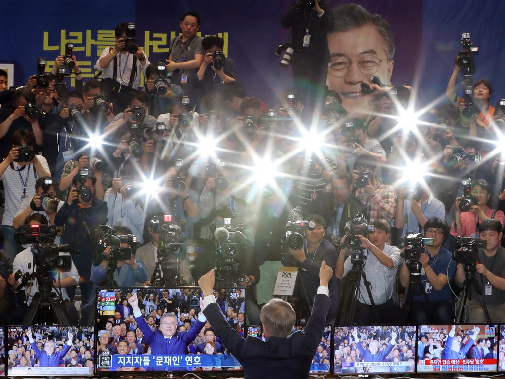 South Korea's presidential candidate Moon Jae-in of the Democratic Party raises his hands in front of the media as his party leaders, members and supporters watch on television local media's results of exit polls for the presidential election at Nati